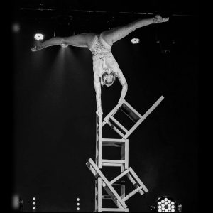 chair balancing act, chair stacking acrobat, equilibrist chair act, contortionist performance, circus balancing act, female acrobat show, luxury event entertainment, contemporary circus act, acrobatic chair tower, stage acrobatics show